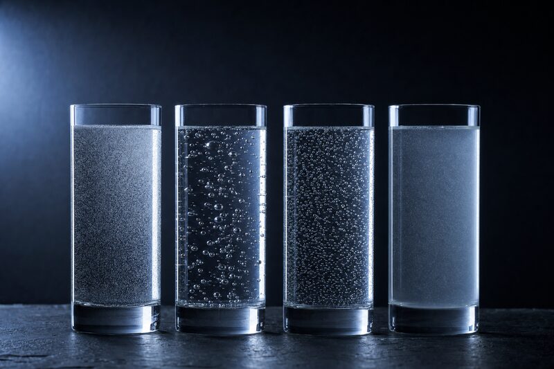 Quattro bicchieri identici affiancati, ognuno con un'acqua gassata differente, distinguibili soltanto per la dimensione e la densità delle bolle.